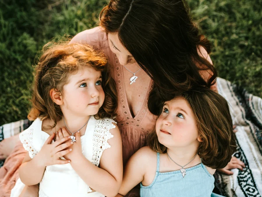 Mother and two daughters wearing coordinating engraved heart necklaces outdoors